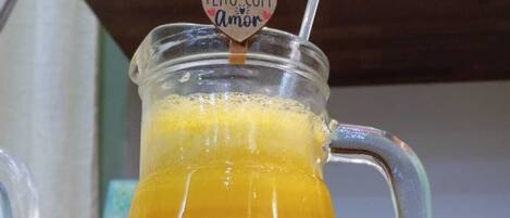 A glass pitcher filled with a yellow beverage, possibly lemonade, with a heart-shaped label that reads "FEITO COM Amor".