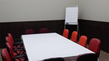 Un salón de conferencias con una larga mesa, sillas rojas, una pizarra y suelo alfombrado.
