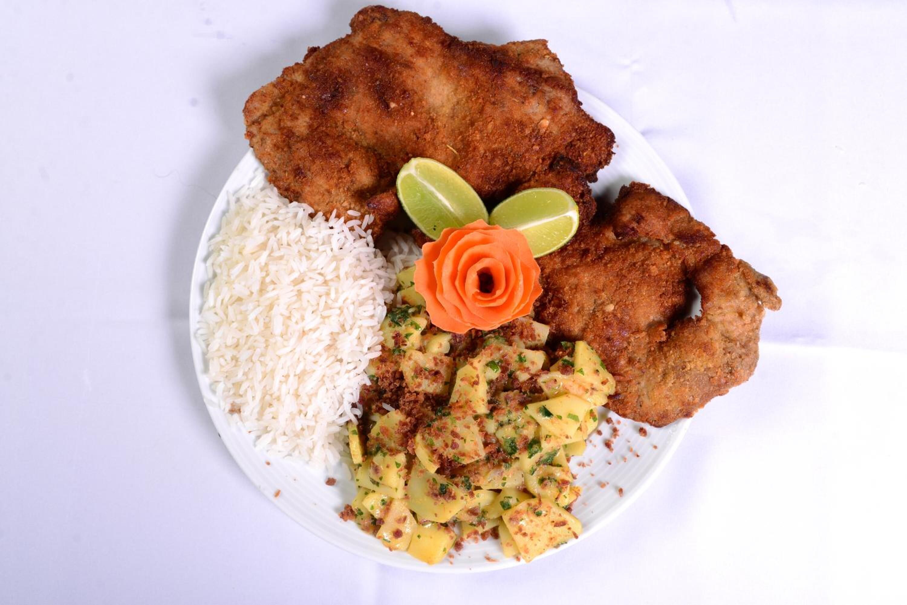 A plate with fried chicken, rice, and a side dish, garnished with lime and a rose.