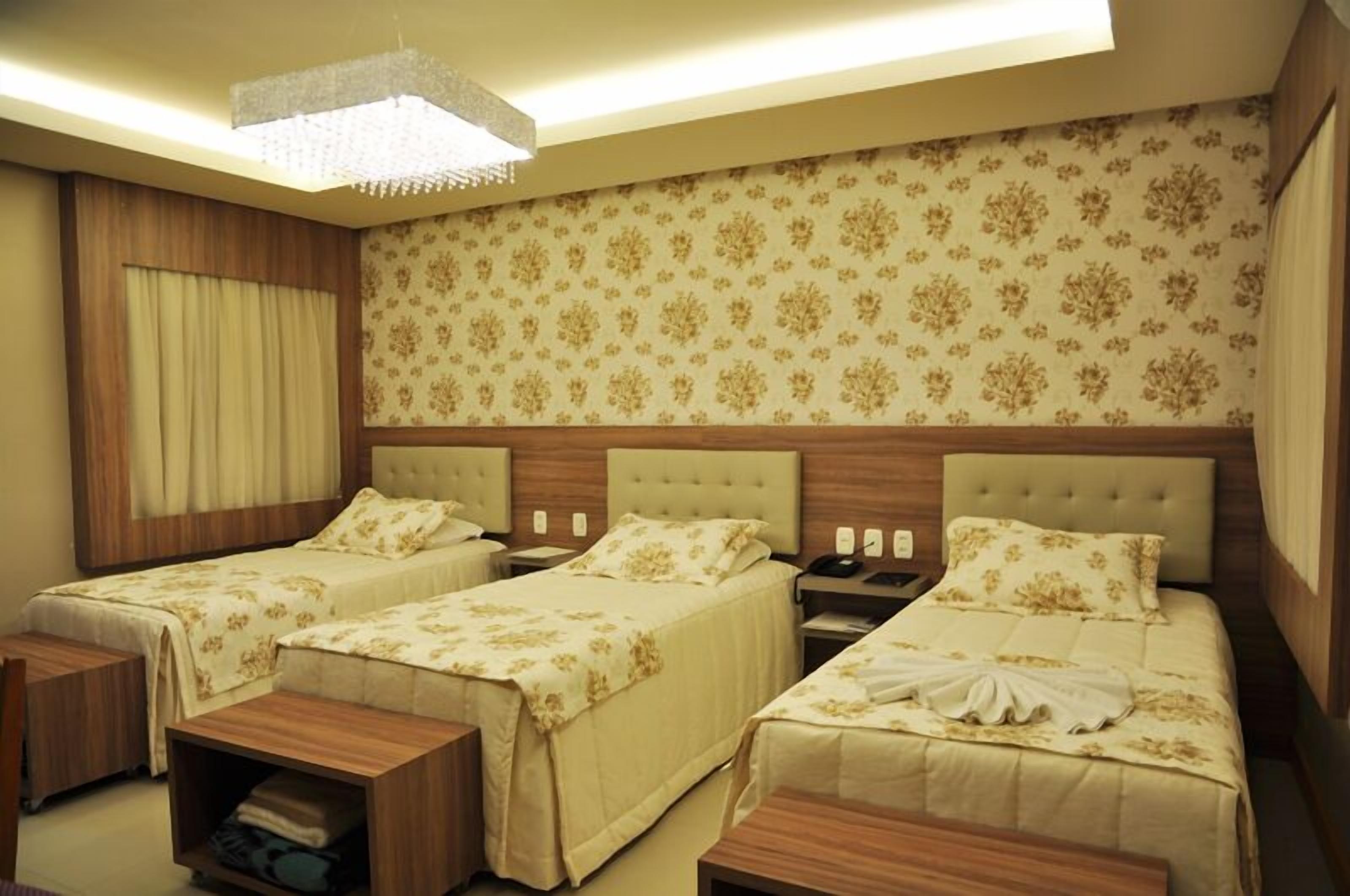 A hotel room with three beds, wooden headboards, and a chandelier.