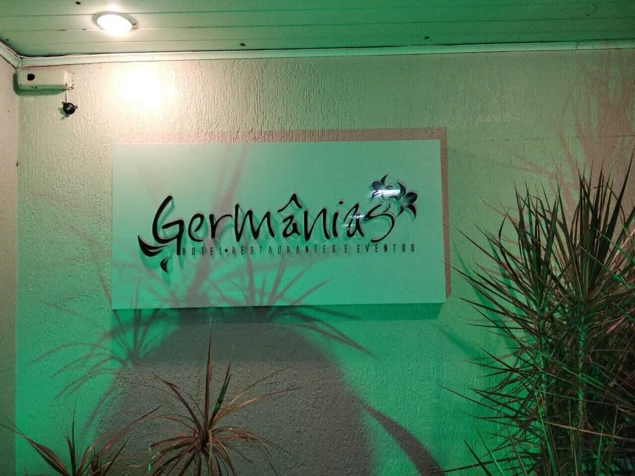 A sign for 'Germanias Hotel, Restaurante & Eventos' with a shadow of a plant on the wall.