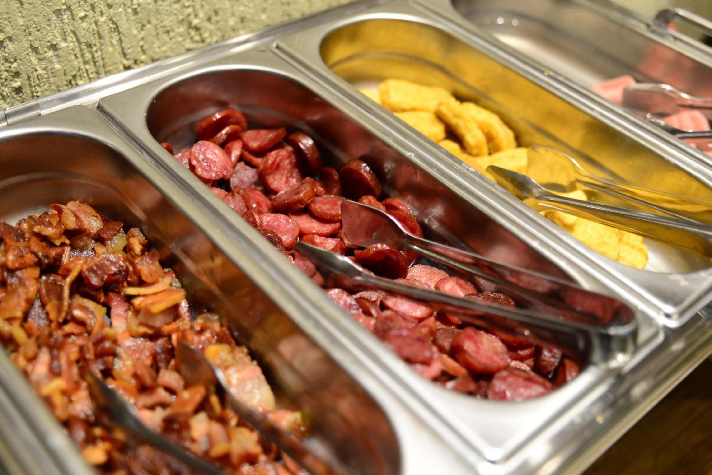 Un buffet proposant une variété de plats, notamment du bacon, des saucisses et d’autres viandes.