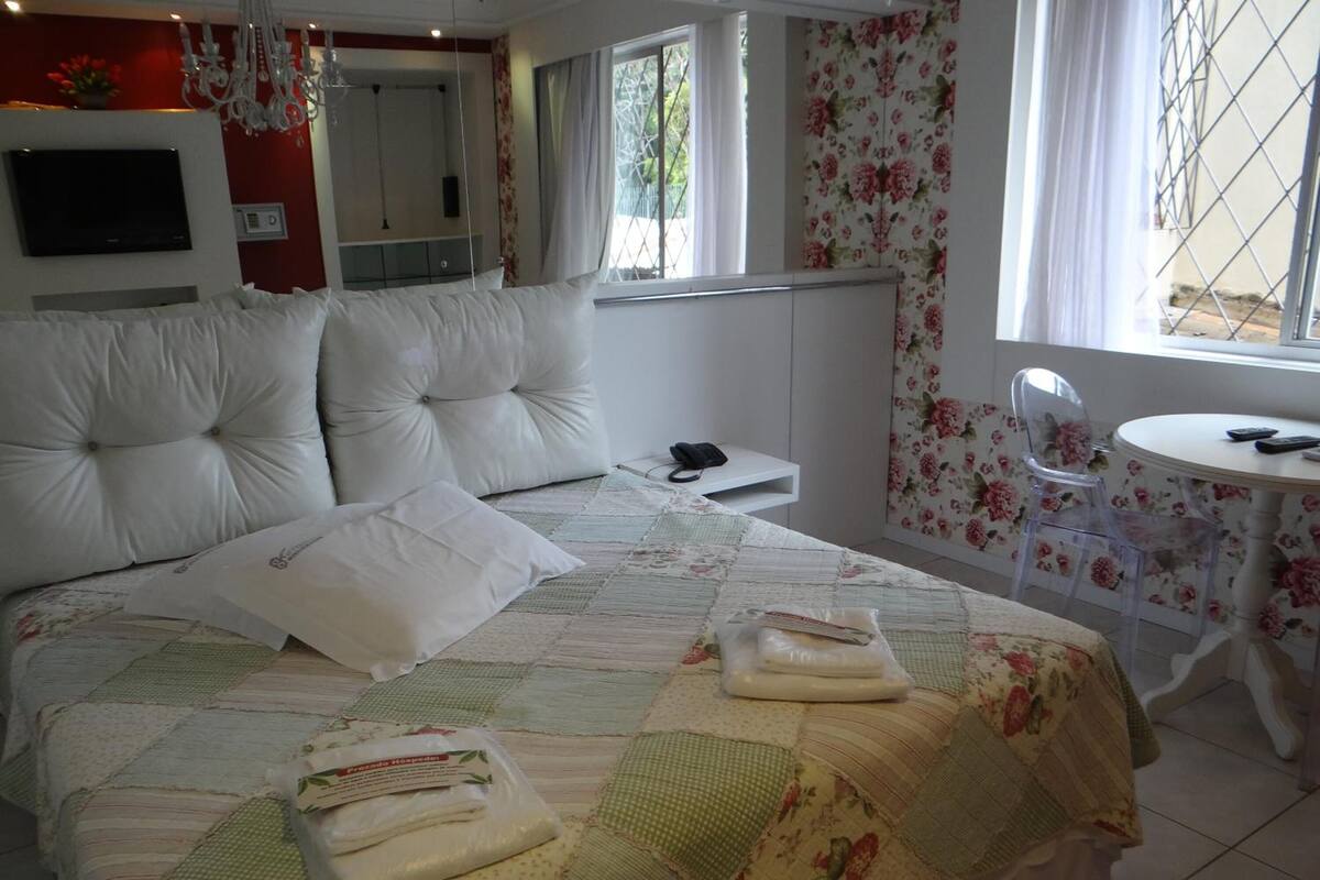 Un dormitorio con una cama grande, una mesita de noche con un teléfono, una silla y una pequeña mesa con mantel de flores.