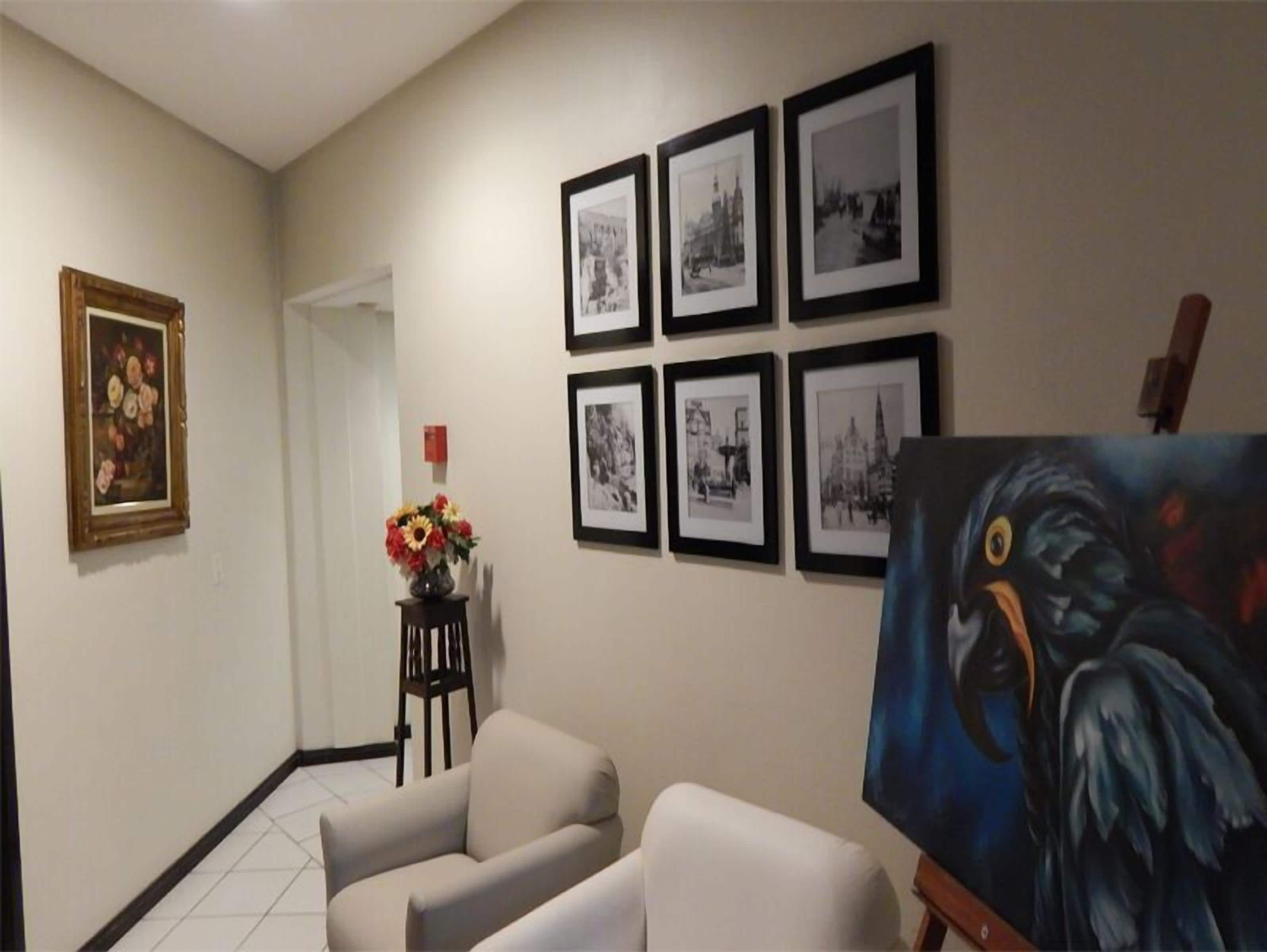 A hallway with framed black and white photographs on the wall, a painting on an easel, and a vase of flowers on a small table.