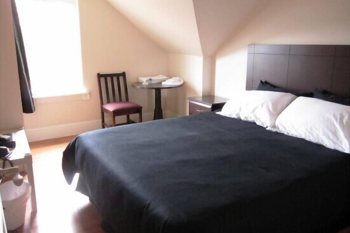 A bedroom with a bed, a chair, a small table, and a window.