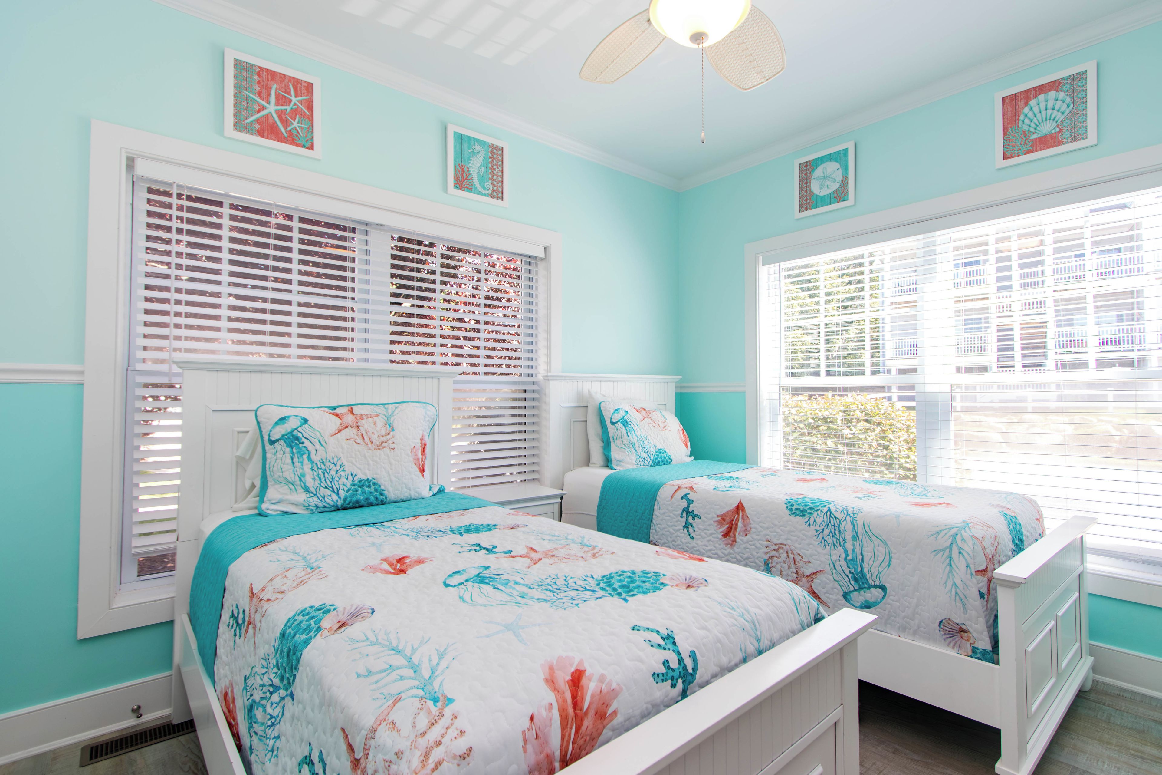 A bedroom with two beds, white headboards, and a large window with blinds.