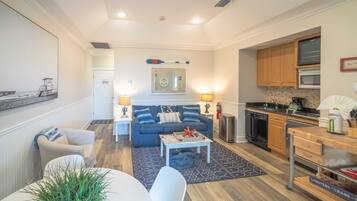 A living room with a sofa, coffee table, and a dining area with a table and chairs. There is a kitchen with appliances and cabinets.