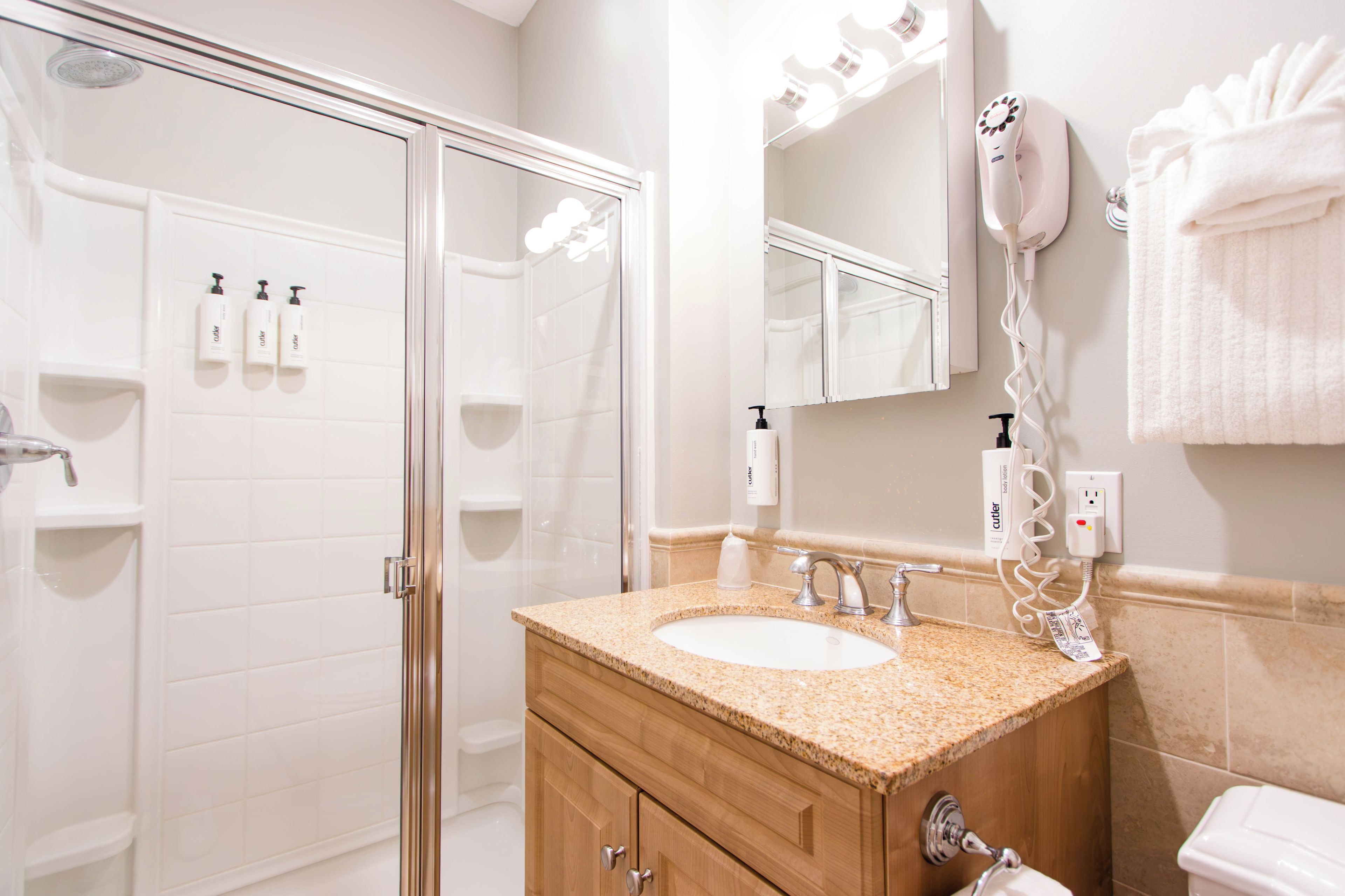 Une salle de bain dotée d’une douche à paroi de verre, d’un lavabo avec un plan de travail en granit et d’un meuble-lavabo avec un miroir.