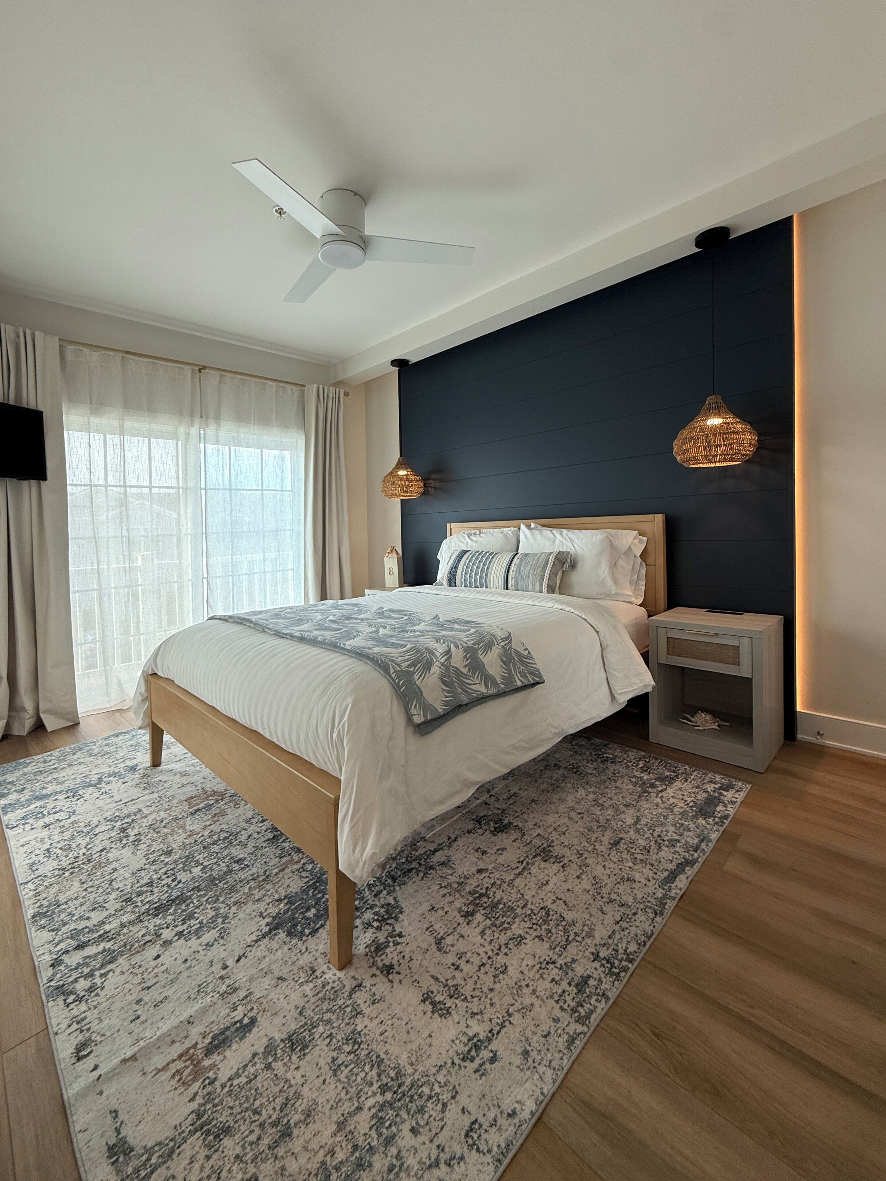 A modern bedroom with a bed, a ceiling fan, a nightstand, and a wall-mounted lamp.