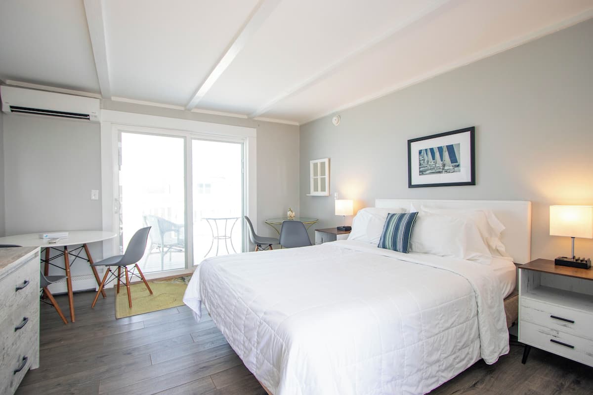 A hotel room with a bed, a desk, a chair, a small table, and a window.