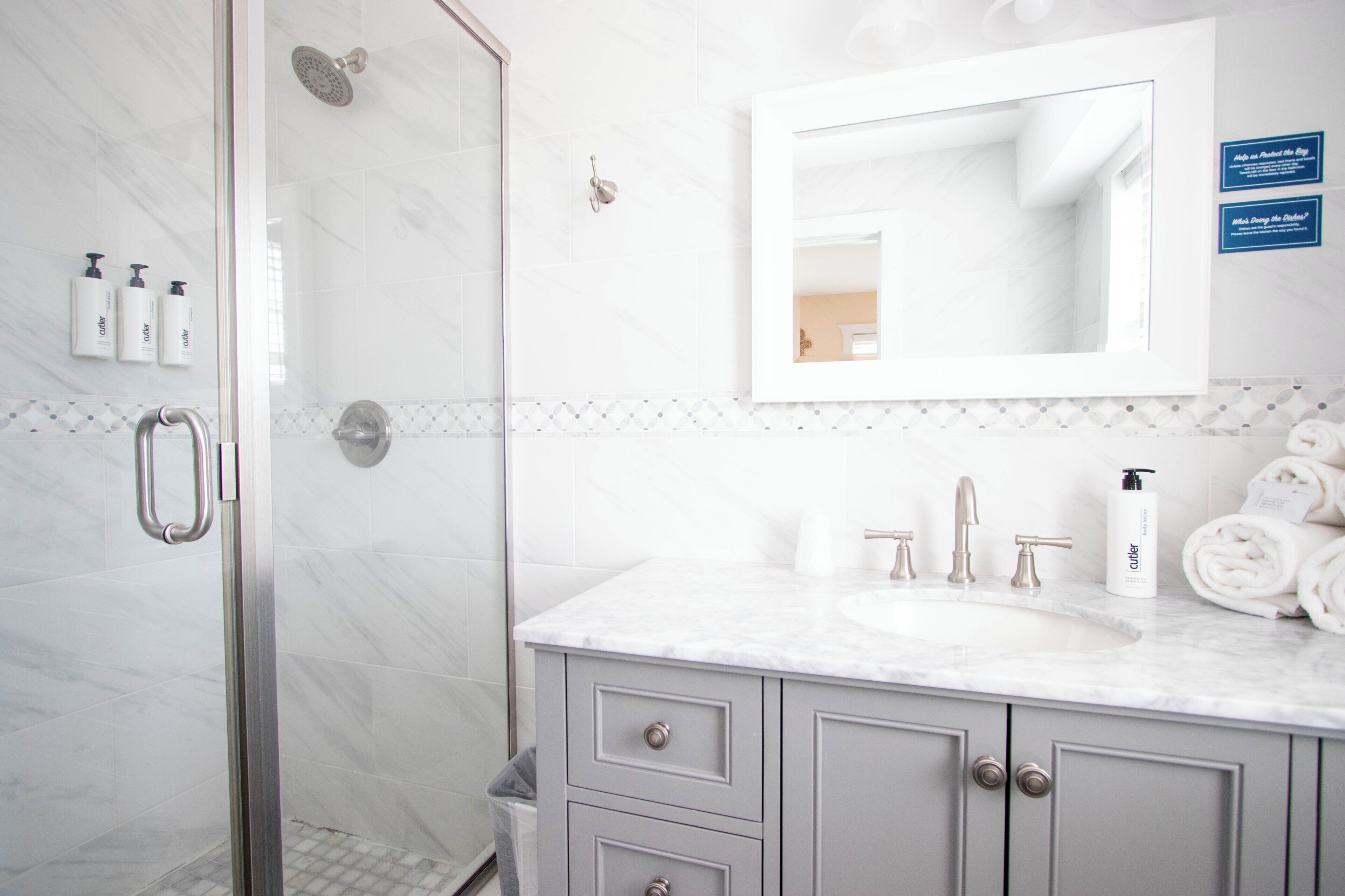 A modern bathroom with a glass shower enclosure, a marble sink, and a vanity with storage drawers.