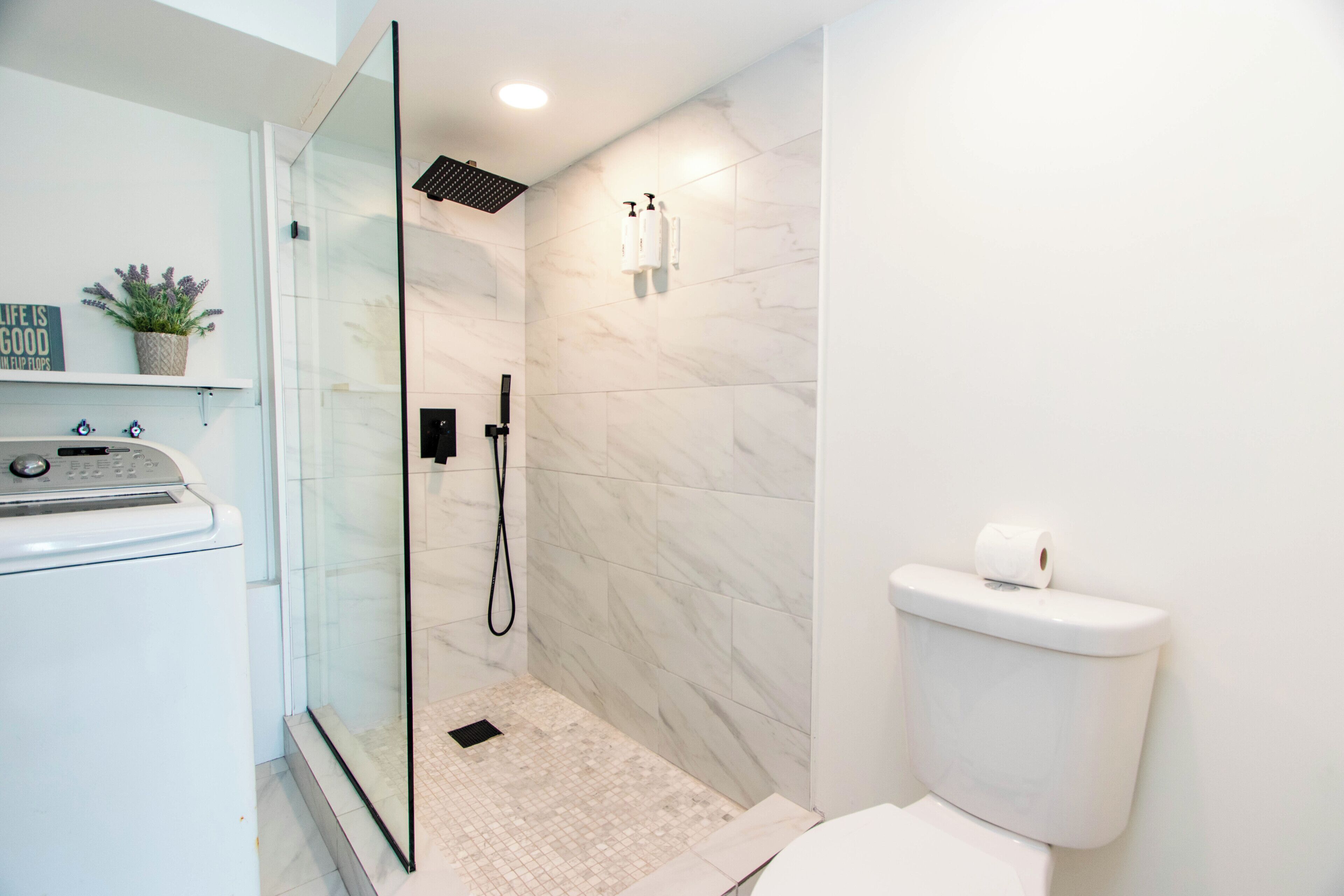 A modern bathroom with a glass-enclosed shower, a toilet, and a washing machine.
