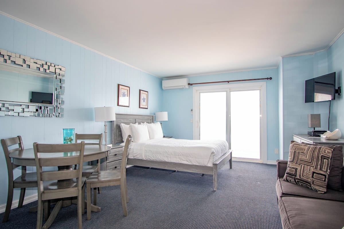 A room with a bed, a desk, and a chair. There is a window with a view of the outside.