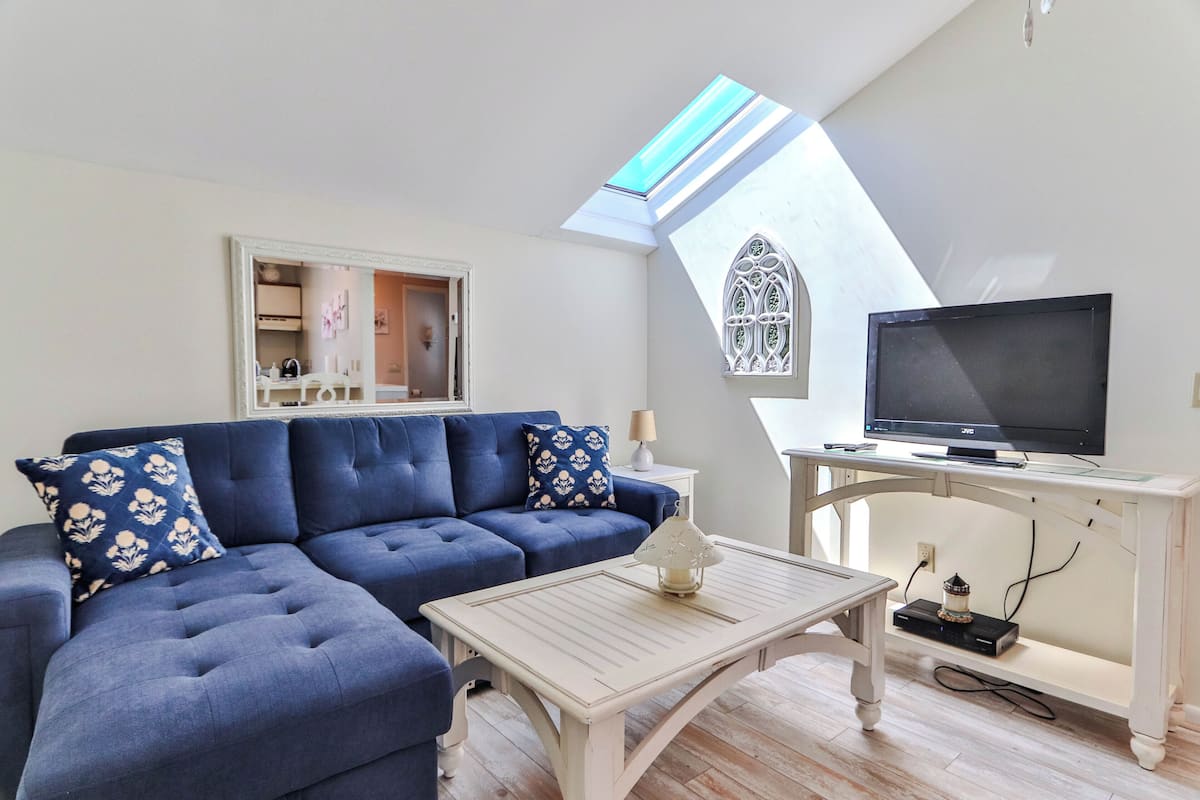 A living room with a blue sofa, a white coffee table, a TV on a stand, and a skylight.