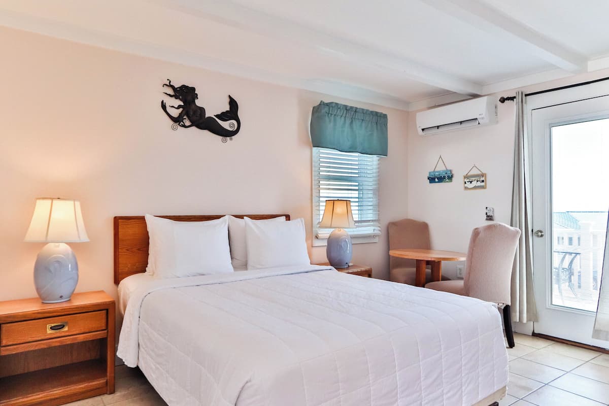 A bedroom with a bed, bedside tables, a chair, a window with blinds, and a wall decoration.