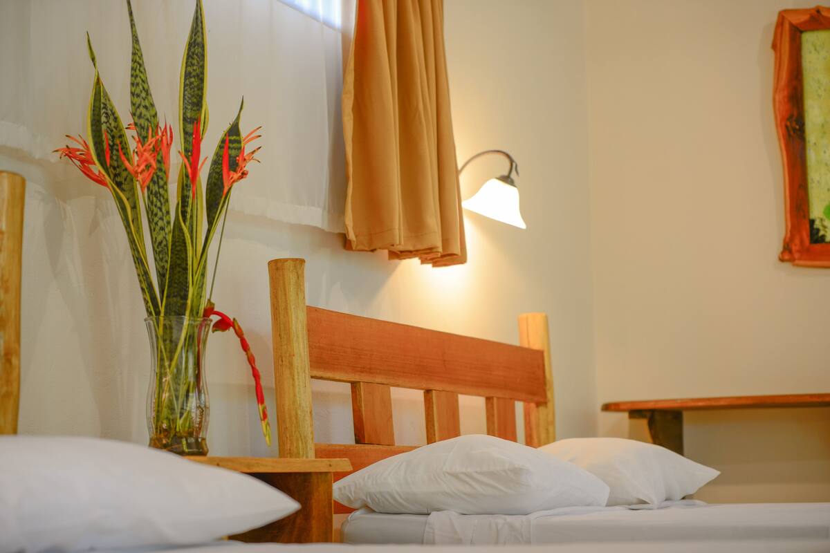 A hotel room with a wooden headboard, a bedside table, a lamp, and a vase with flowers.