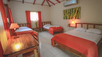 A room with three beds, a wooden table, and a painting on the wall.