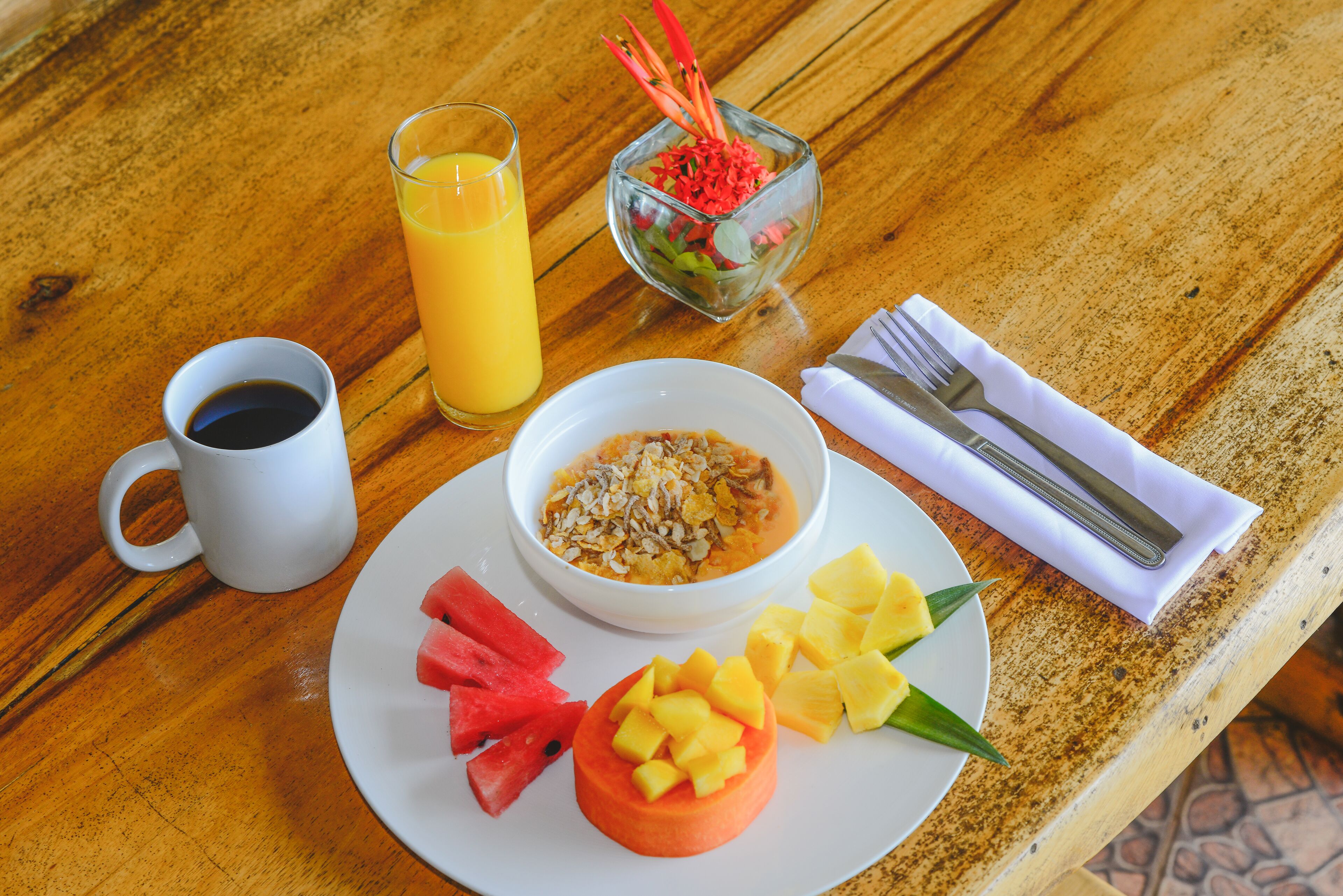 Un desayuno con un plato de comida, un vaso de zumo de naranja, una taza de café y un bol pequeño de ensalada de frutas.