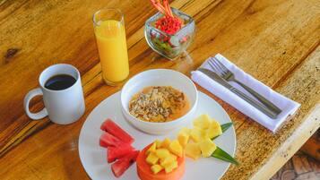 Un desayuno con un plato de comida, un vaso de zumo de naranja, una taza de café y un bol pequeño de ensalada de frutas.