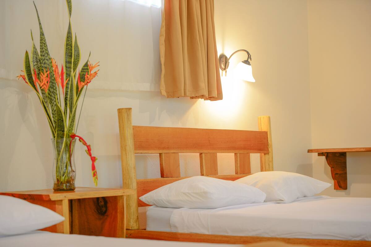 A neatly made bed with white linens, a wooden headboard, and a bedside table with a vase of flowers.