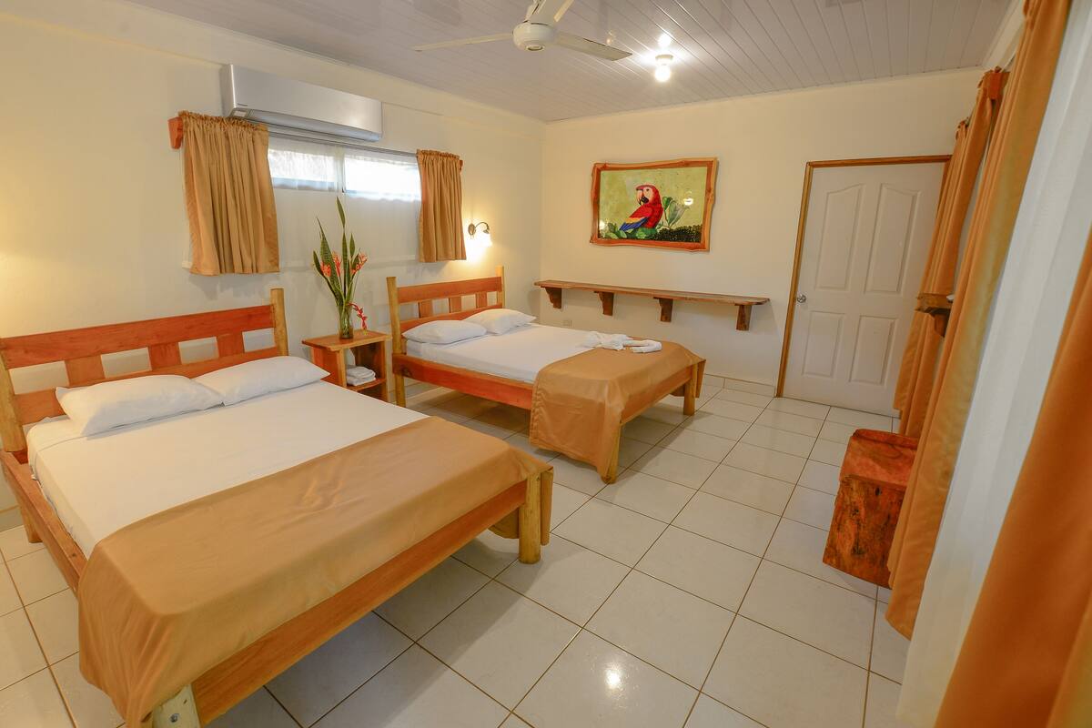 A hotel room with two wooden beds, a ceiling fan, a painting of a parrot, and a door.