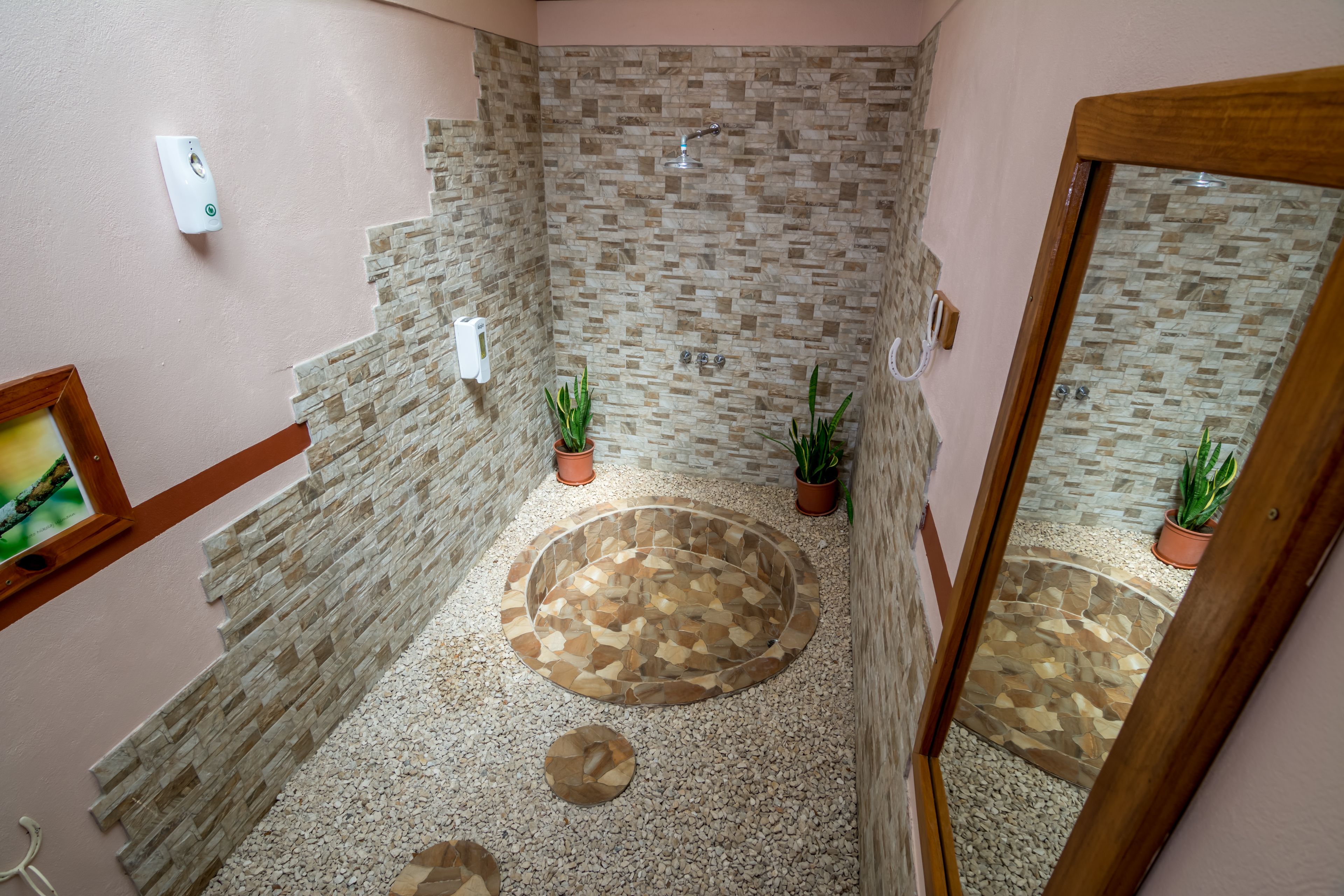 A bathroom with a stone mosaic shower, a small circular hot tub, and two potted plants.