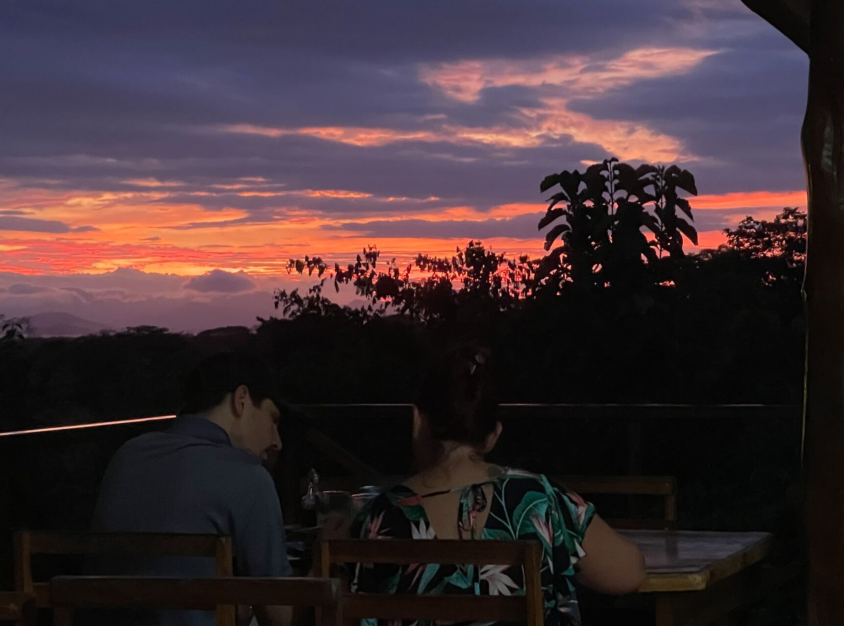 Una pareja cenando en una mesa al aire libre con vistas a un atardecer.