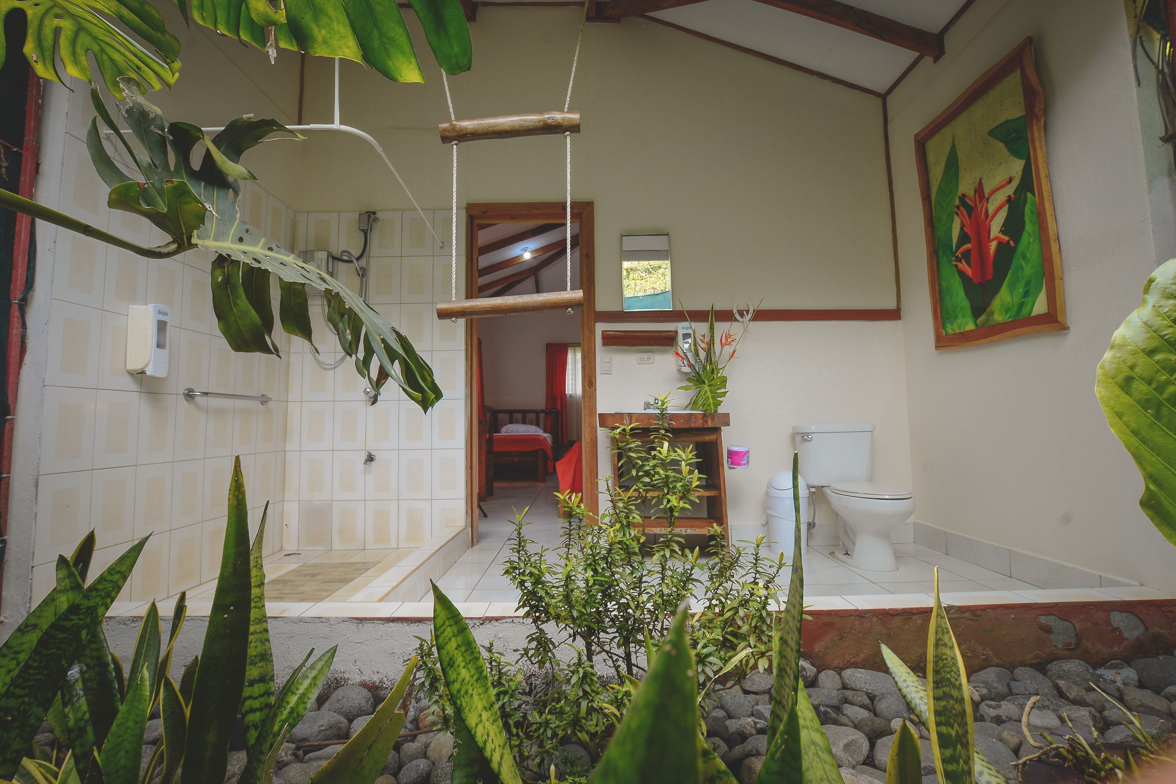 Une salle de bain équipée d’une douche, de toilettes et d’un lavabo, entourée de plantes tropicales.