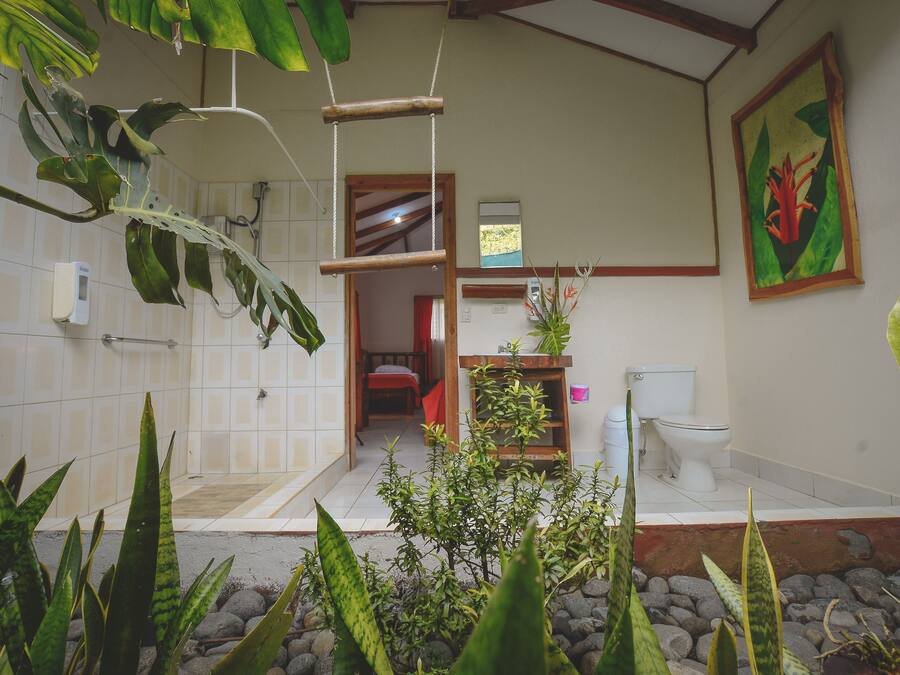 A bathroom with a shower, toilet, and sink, surrounded by tropical plants.