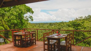 A wooden deck with tables and chairs overlooking a lush green landscape. - Hotel Cerro Lodge (Lagunillas)