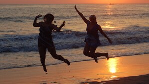 Zwei Personen springen bei Sonnenuntergang an einem Strand.