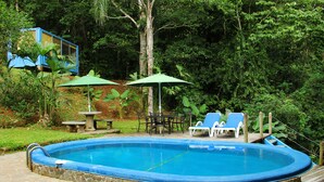 Ein Pool mit Steinfliesen, umgeben von einer Holzterrasse und beschattet durch zwei Sonnenschirme.