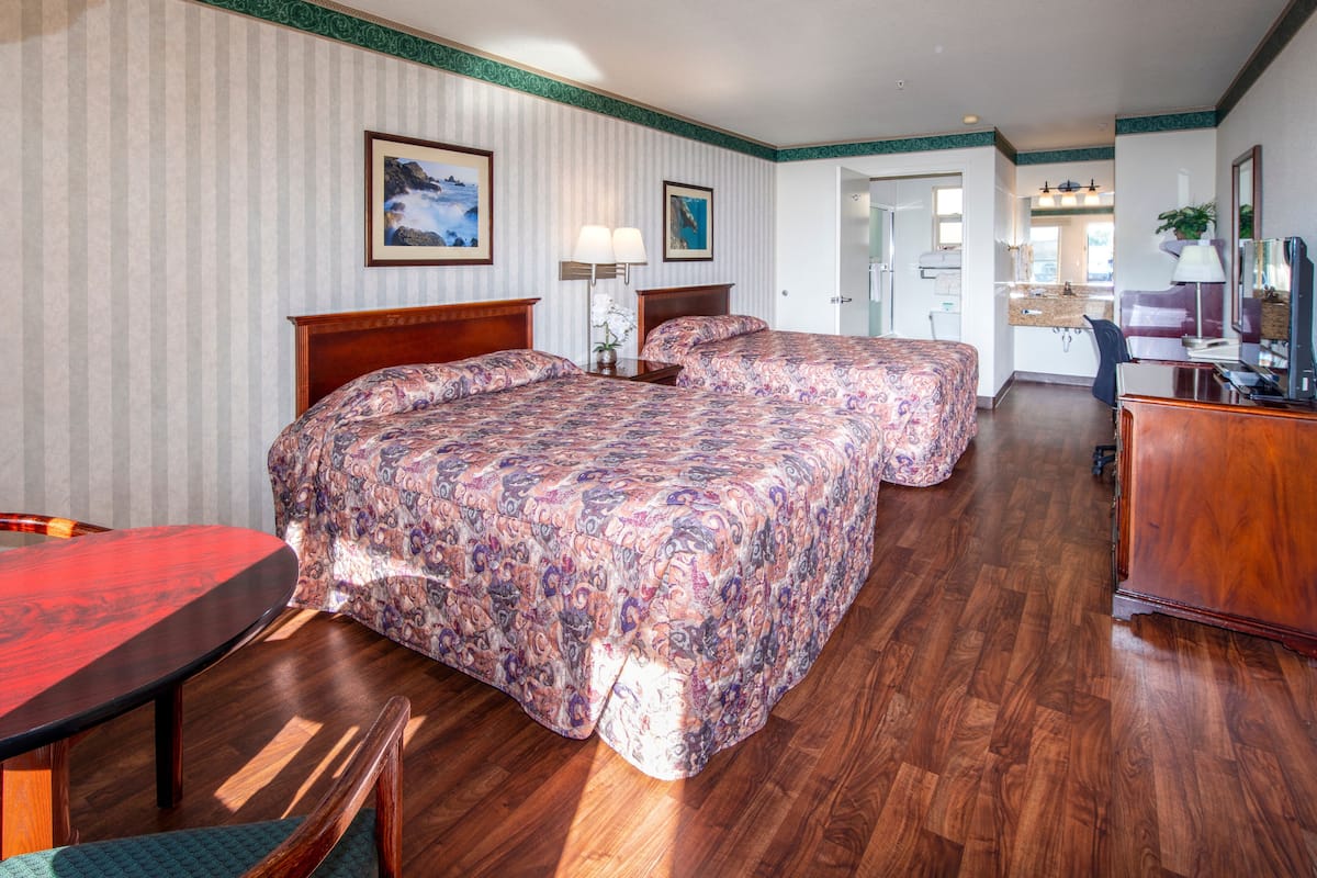 Quarto de hotel com duas camas, uma mesa de jantar de madeira e uma kitchenette.