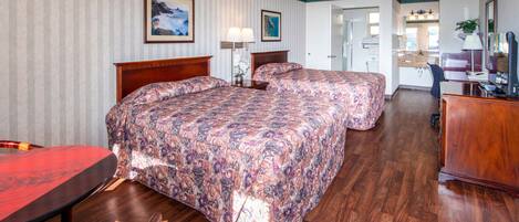 A hotel room with two beds, a wooden dining table, and a kitchenette.