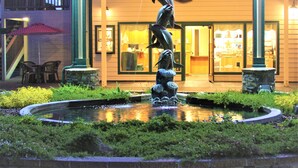 A fountain with dolphins, a stone wall, and a building with a balcony and outdoor seating. - Emerald Dolphin Inn & Mini Golf (Fort Bragg)