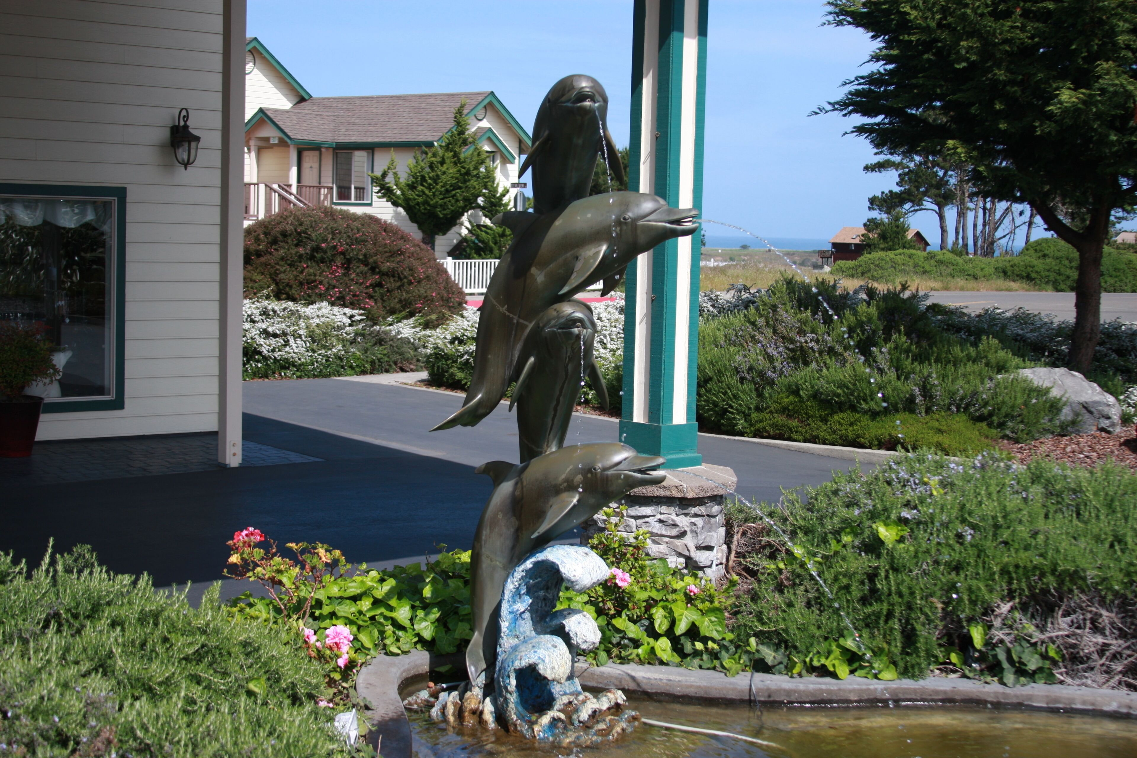 Une statue de dauphin dans un jardin, avec une maison en arrière-plan.