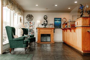 A living room with a fireplace, green armchairs, a wooden cabinet, and a bookshelf.