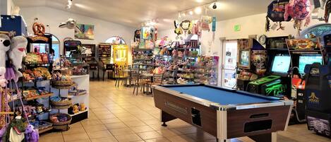 A brightly lit indoor space with a pool table, arcade games, and various toys and snacks.