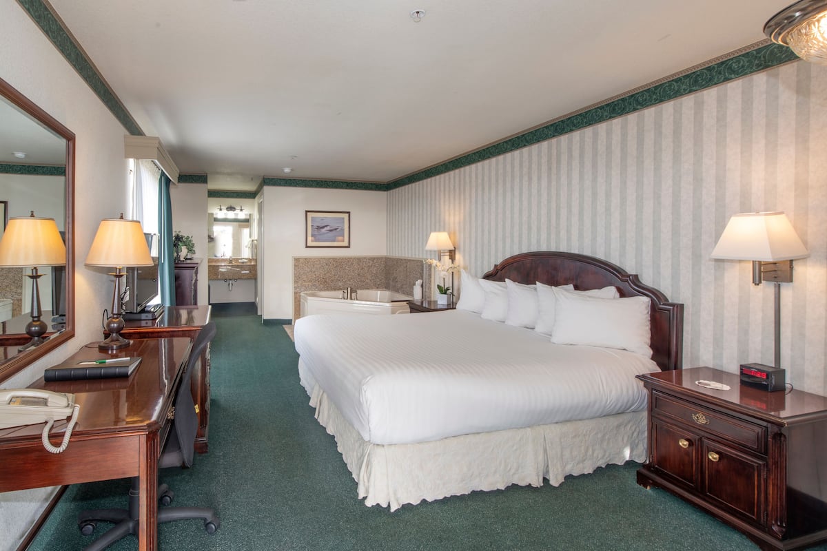 Quarto de hotel com uma cama grande, duas mesas de cabeceira com luminárias, uma escrivaninha com telefone e um espelho.