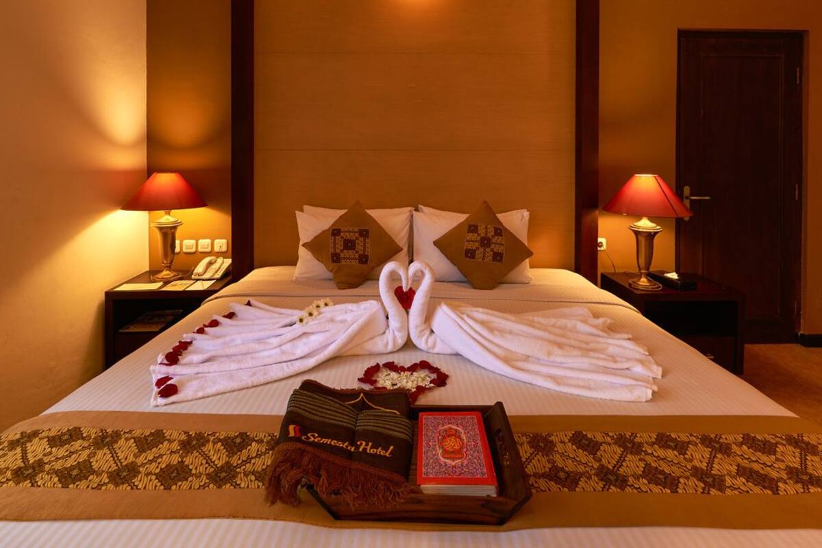 A neatly made bed with towels arranged in a swan shape, a book, and a decorative pillow on a bedspread.