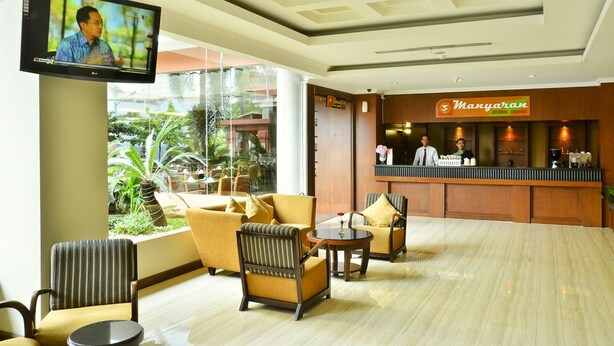 A hotel lobby with a reception desk, comfortable seating area, and a television screen. - Phi Semesta (Semarang)