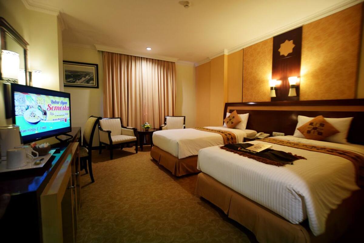 A hotel room with two beds, a desk with a television, a chair, and a small table.