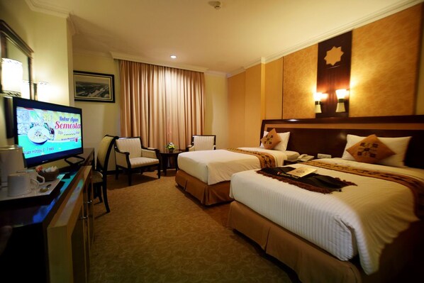 Habitación de hotel con dos camas, un escritorio con televisor, una silla y una mesita.