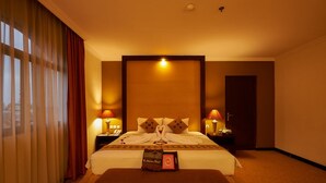 A hotel room with a large bed, two bedside lamps, a nightstand, and a window with curtains. - Phi Semesta (Semarang)