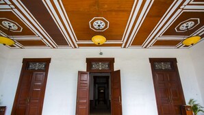 A lobby with wooden doors, a tiled floor, and a decorative ceiling with hanging lamps. - Phi Semesta (Semarang)