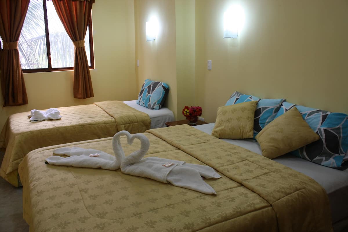 Une chambre d’hôtel avec deux lits, chacun recouvert d’une couvre-lit à motifs floraux et agrémenté d’oreillers. On trouve des serviettes sur les lits, et une serviette décorative en forme de cygne est posée sur le lit situé au premier plan.