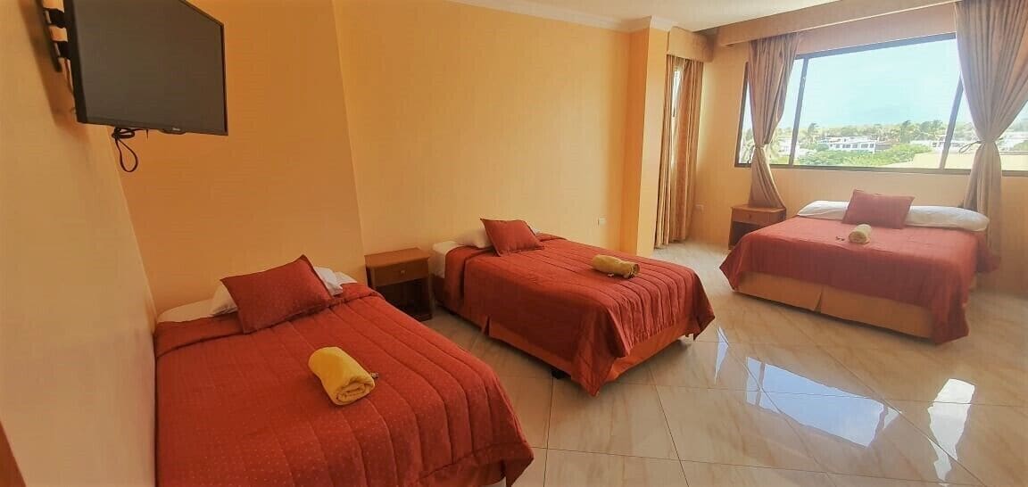 A hotel room with three beds, a flat-screen TV, and a large window with curtains.