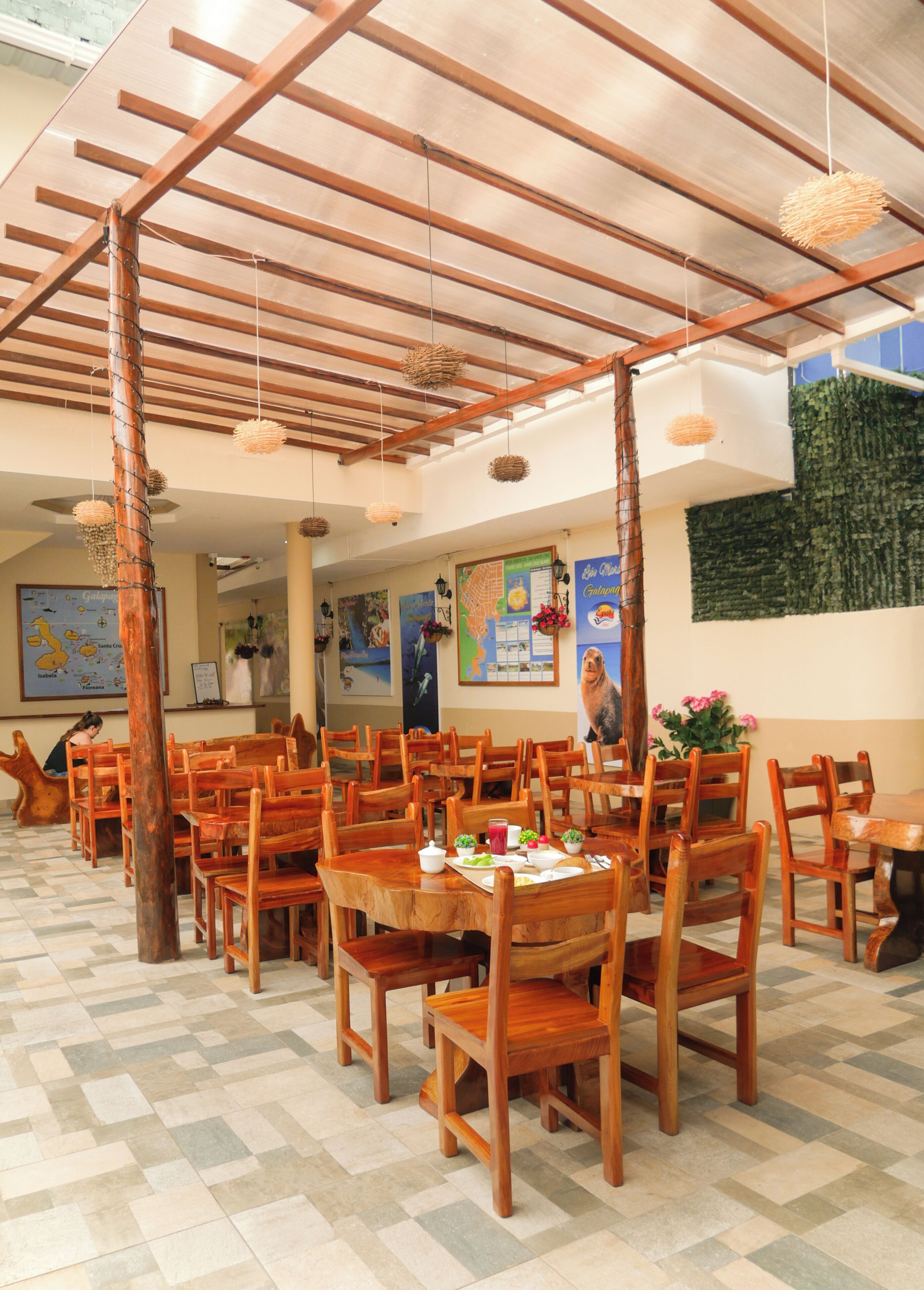 A restaurant with wooden tables and chairs, a high ceiling with wooden beams, and a tiled floor.