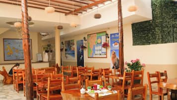 Un restaurante con mesas y sillas de madera, un techo alto con vigas de madera y un piso de baldosas.