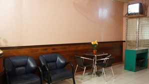 Een wachtruimte met twee lederen fauteuils, een kleine tafel met een bloem en een televisie op een plank.